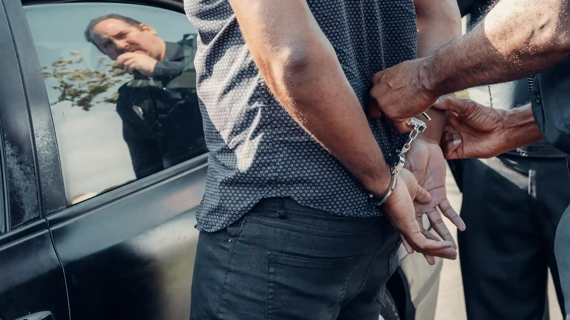 Person being handcuffed beside a car.