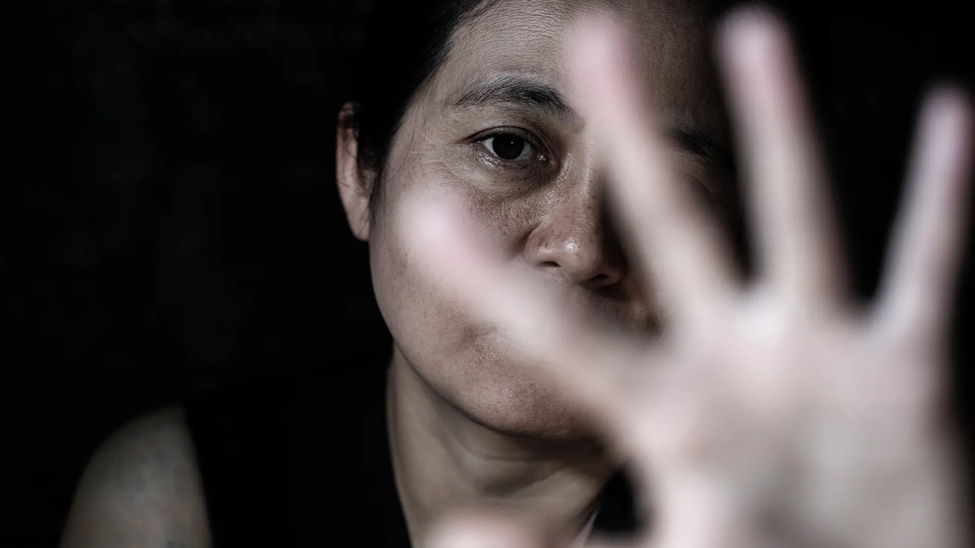 Distressed person holding up hand to the camera in a defensive gesture.