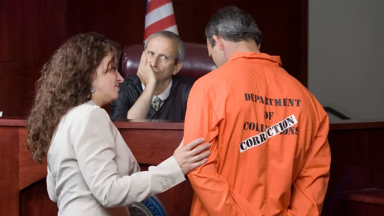 Inmate in orange jumpsuit with lawyer before judge.